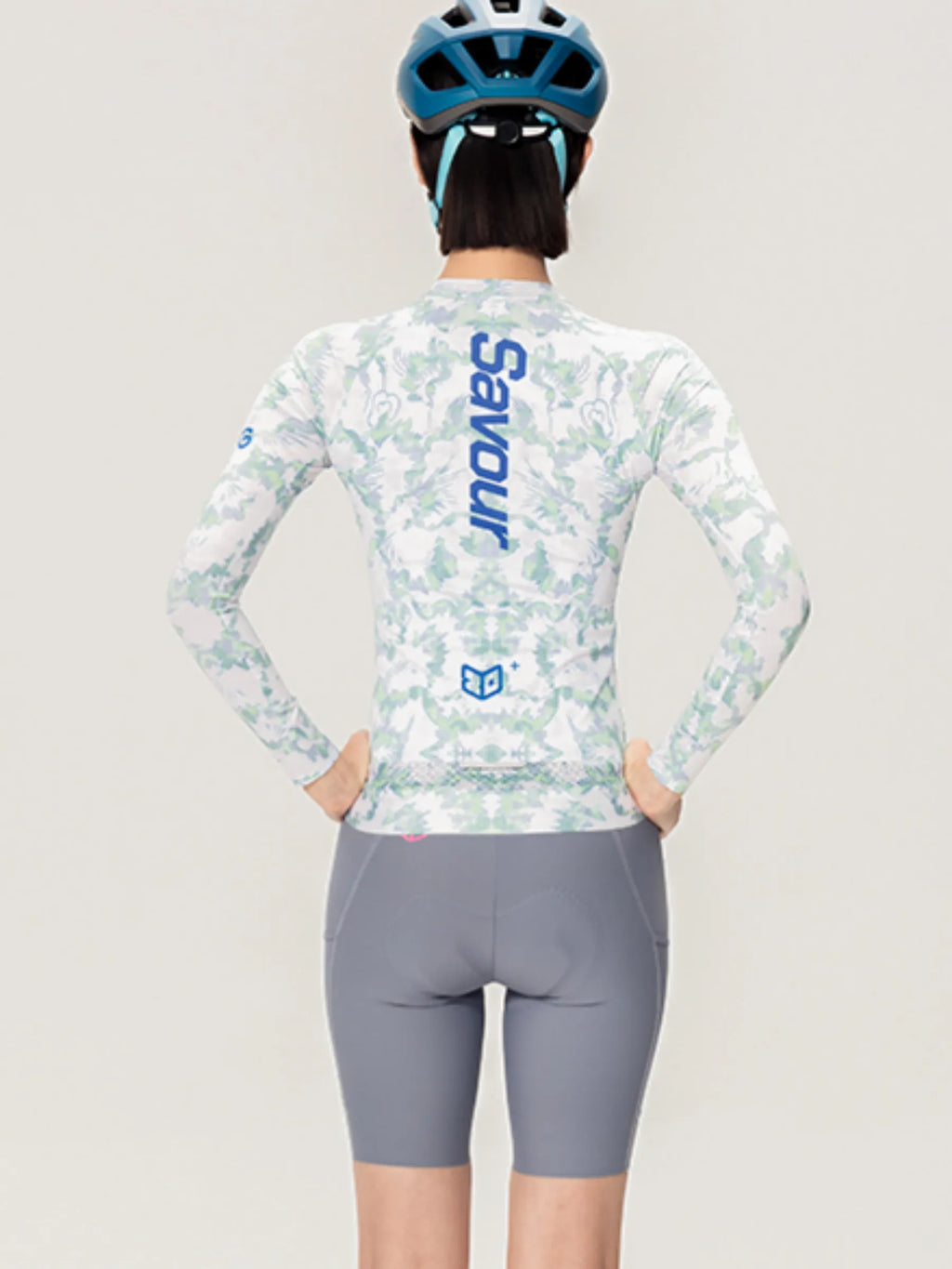 A woman wearing the back of a lameda x australian studio unisex cycling jersey ls in white and light green camouflage with savour branding