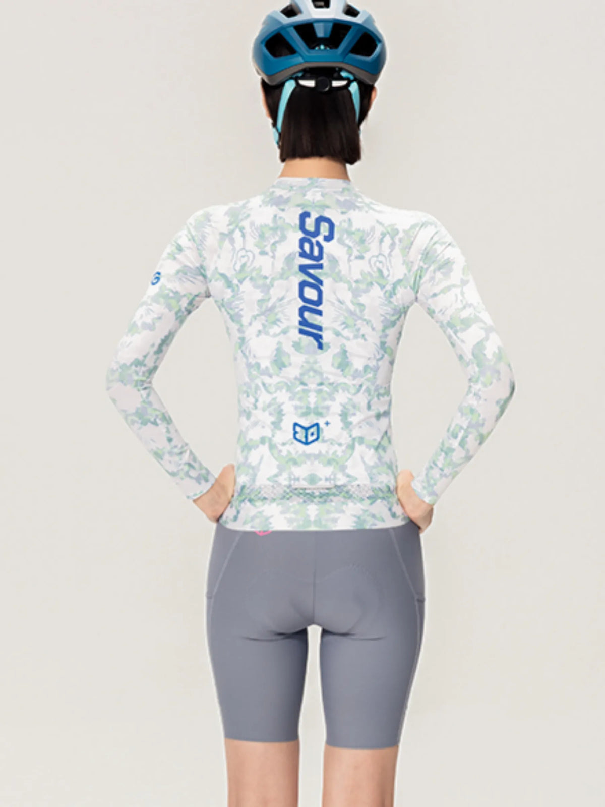 A woman wearing the back of a lameda x australian studio unisex cycling jersey ls in white and light green camouflage with savour branding