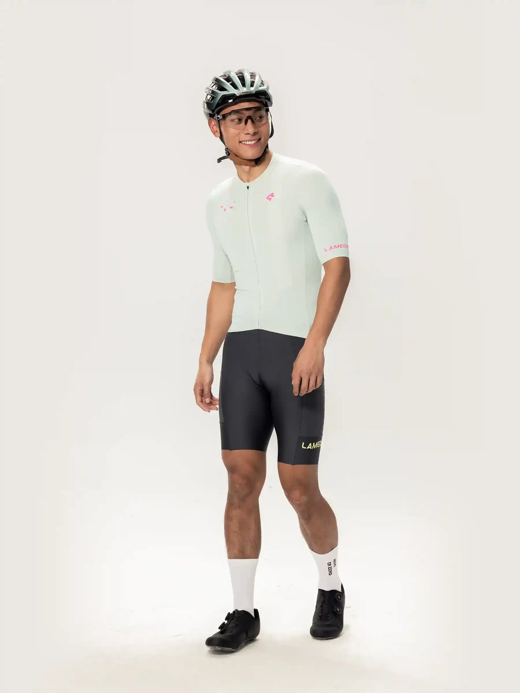 The model wears a light mint green short-sleeved Roam Men cycling jersey with pink branding and black lamer logo shorts