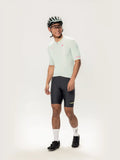 The model wears a light mint green short-sleeved Roam Men cycling jersey with pink branding and black lamer logo shorts