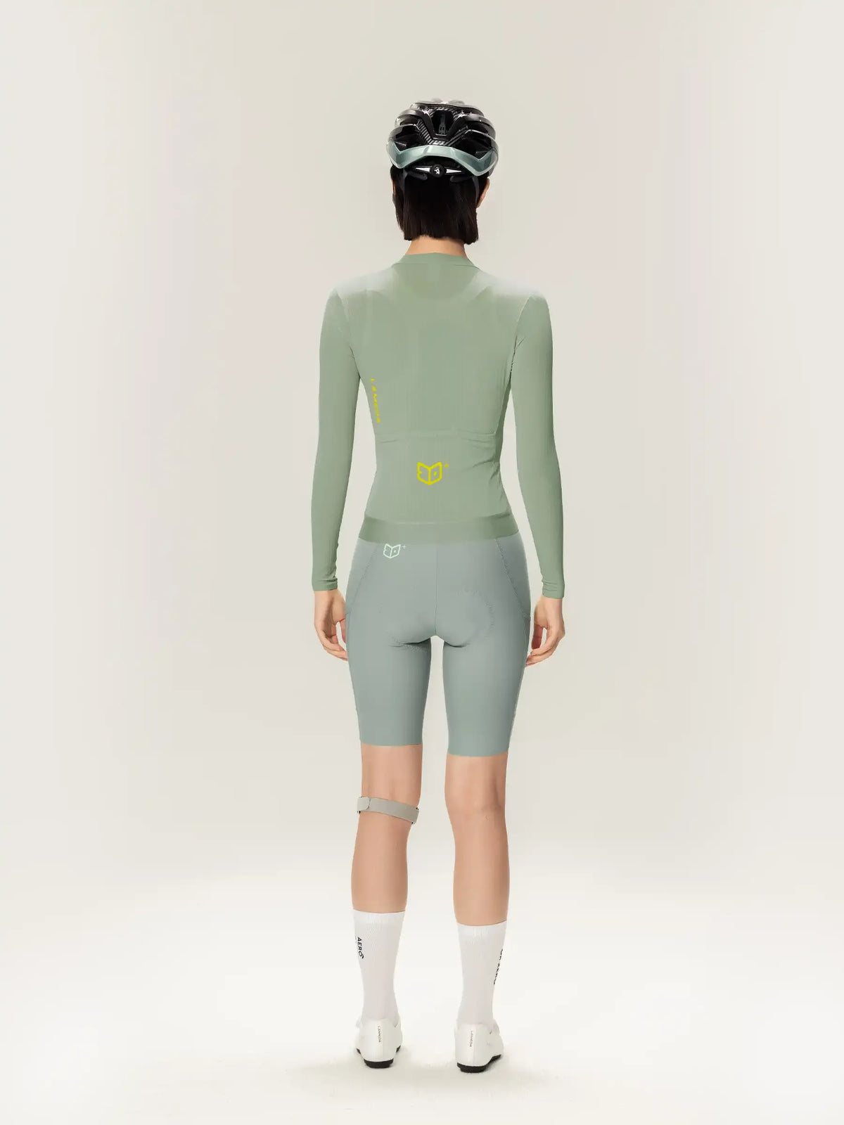 Image of the back side of a sleek sage green roam women long-sleeved cycling jersey with a subtle yellow logo and matching shorts