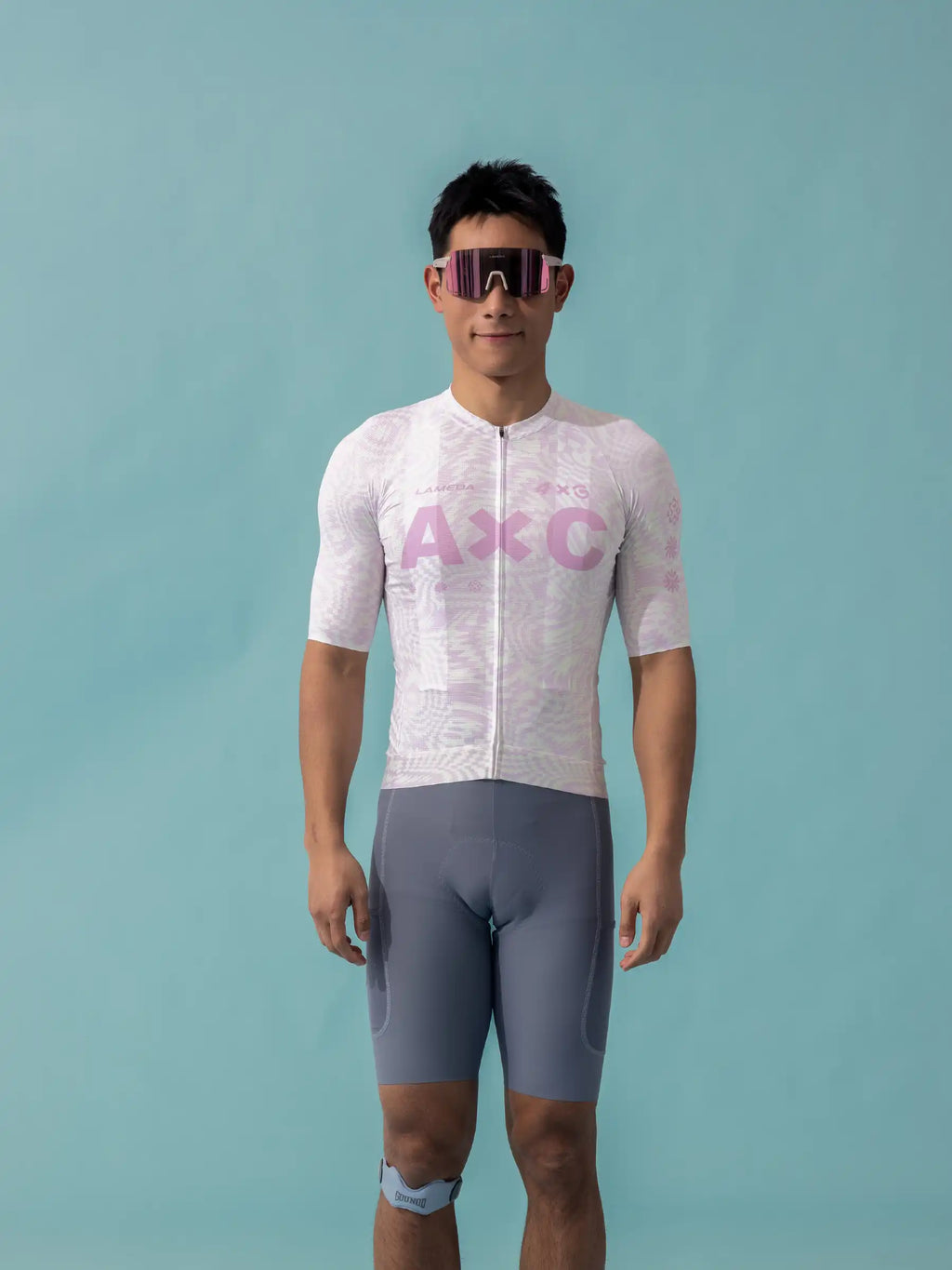 A man wearing a white and pink patterned lameda x australian studio unisex cycling jersey with gray compression shorts