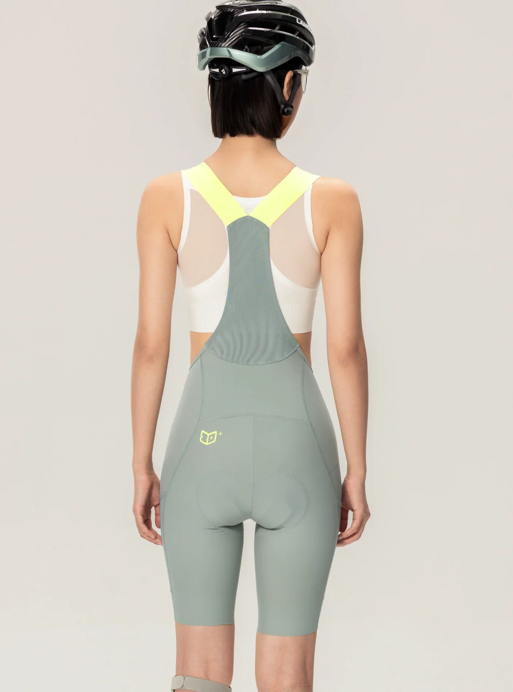 A sleek sage green lameda women’s cycling bib shorts with neon yellow straps and white elastic interface mesh back panel