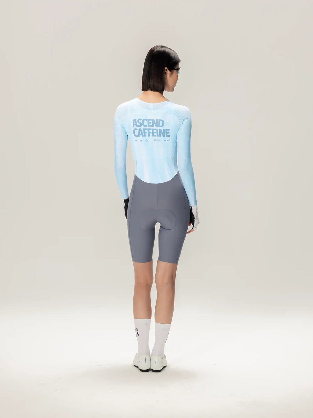 Back view of the lameda a*c women long-sleeved cycling skinsuit in ice blue with ascend caffeine print