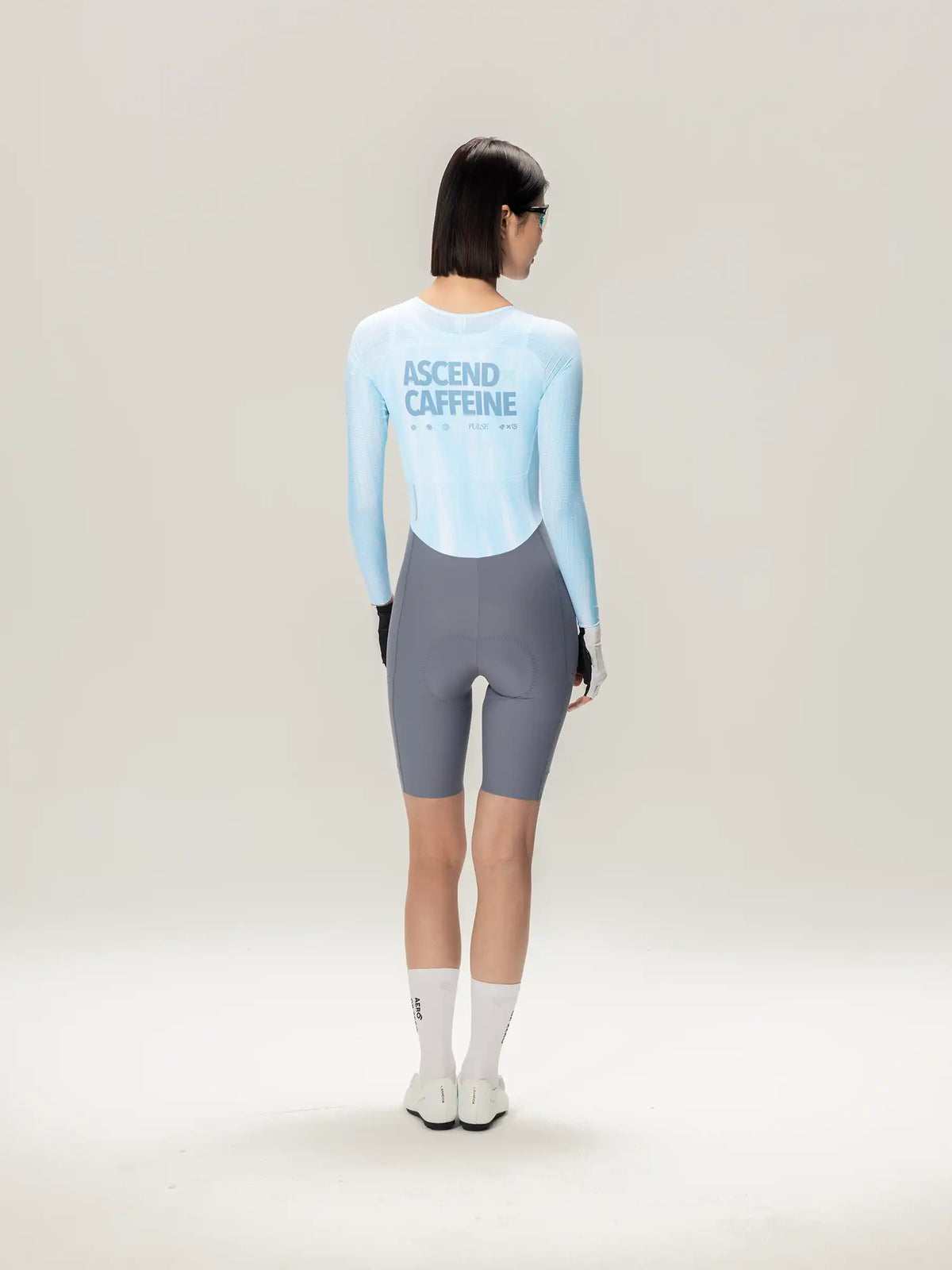 Back view of the lameda a*c women long-sleeved cycling skinsuit in ice blue with ascend caffeine print