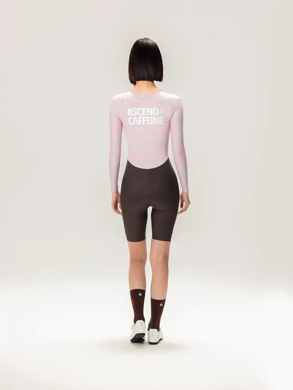 Back view of a pink long sleeved lameda a c women skinsuit with ascend caffeine print paired with dark brown cycling shorts