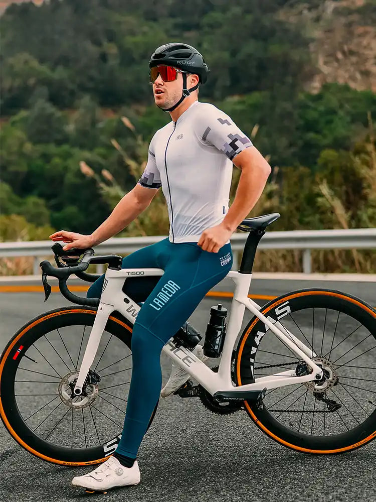 White and orange road bike with black handlebars next to a relaxed fit men’s cycling jersey in white and teal shorts