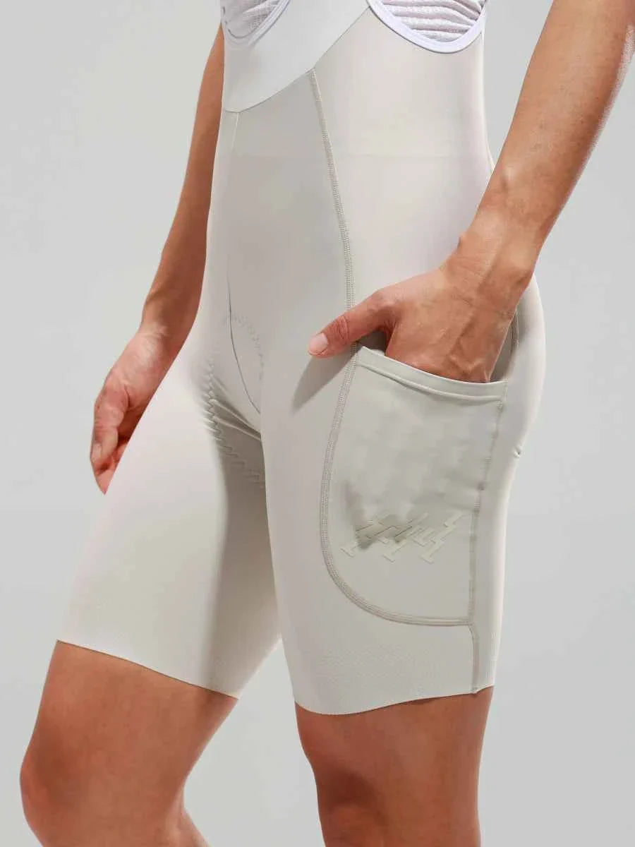 Cream women’s elite bib shorts with built-in side pocket, subtle seam detailing, and breathable mesh waistband