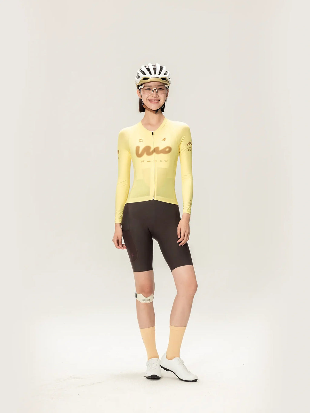 A woman wearing a yellow lameda women’s cycling jersey long sleeve paired with black shorts and matching accessories